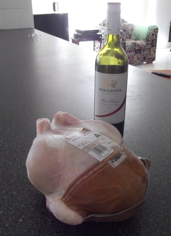 A chicken ready for roasting with a bottle of wine